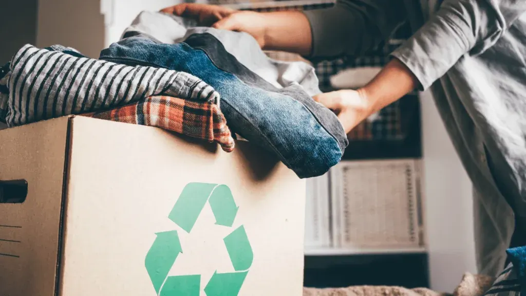 Person placing clothes into a cardboard box with a recycling symbol for decluttering and giving away items in Dubai