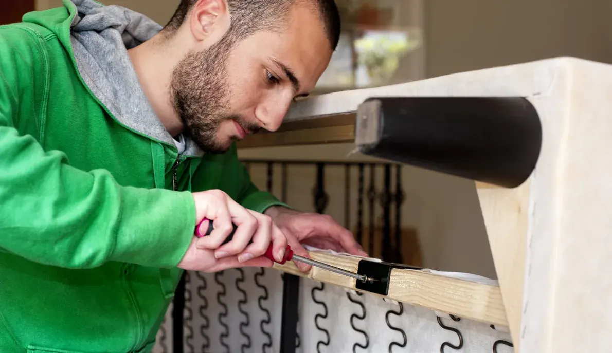 Man in a green hoodie using a screwdriver on a wooden frame with a metal bracket Man in a green hoodie using a screwdriver on a wooden frame with a metal bracket