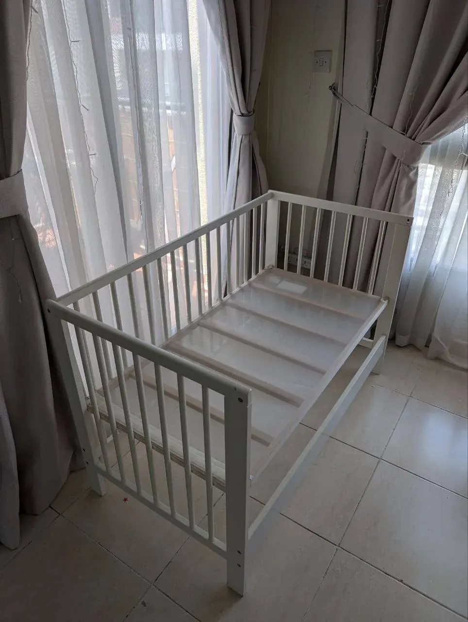 Simple white baby crib in a bright room, suggesting gently used baby furniture available to pass on in Dubai
