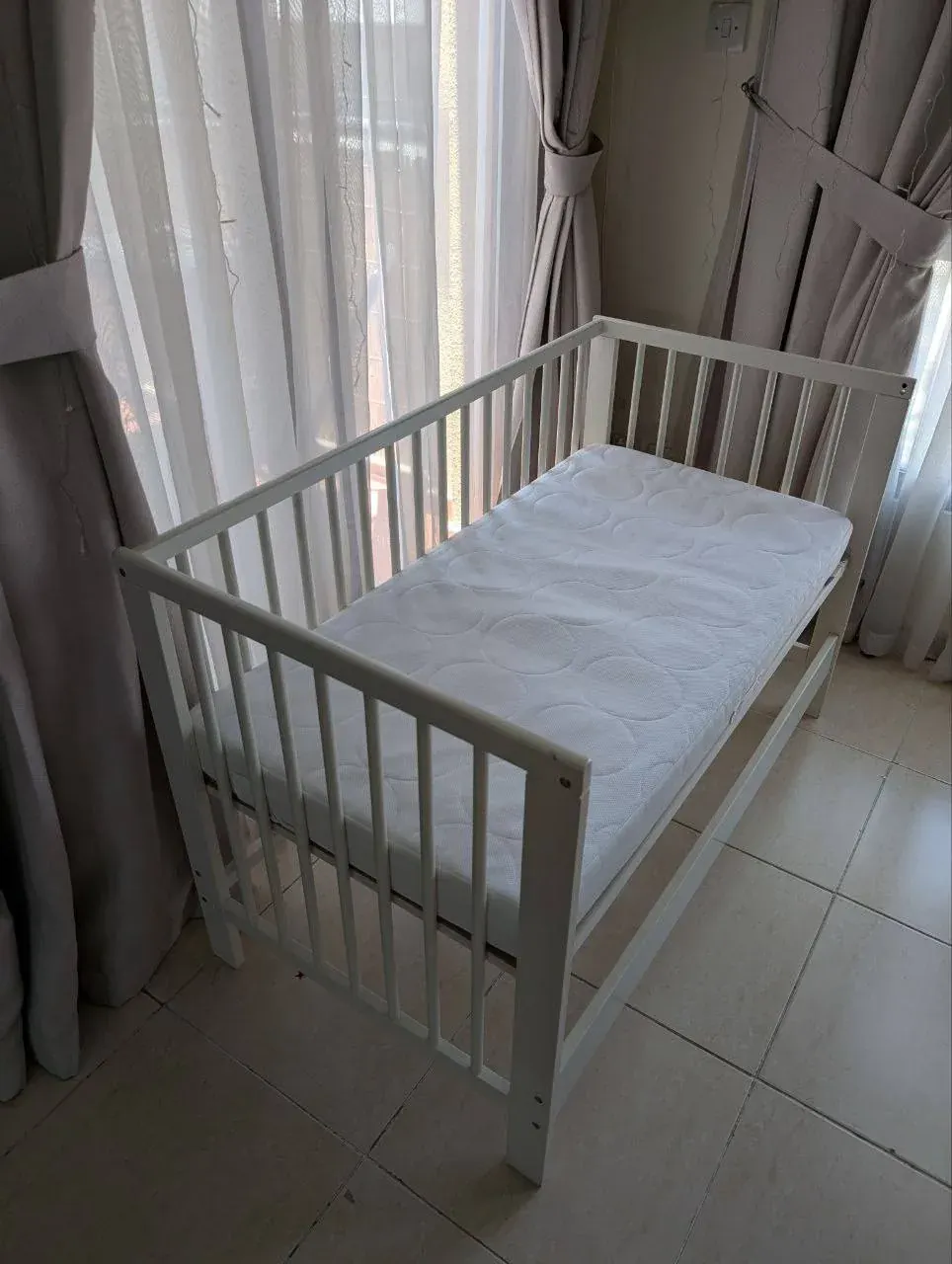 White wooden baby crib with mattress in a bright room in Ajman home