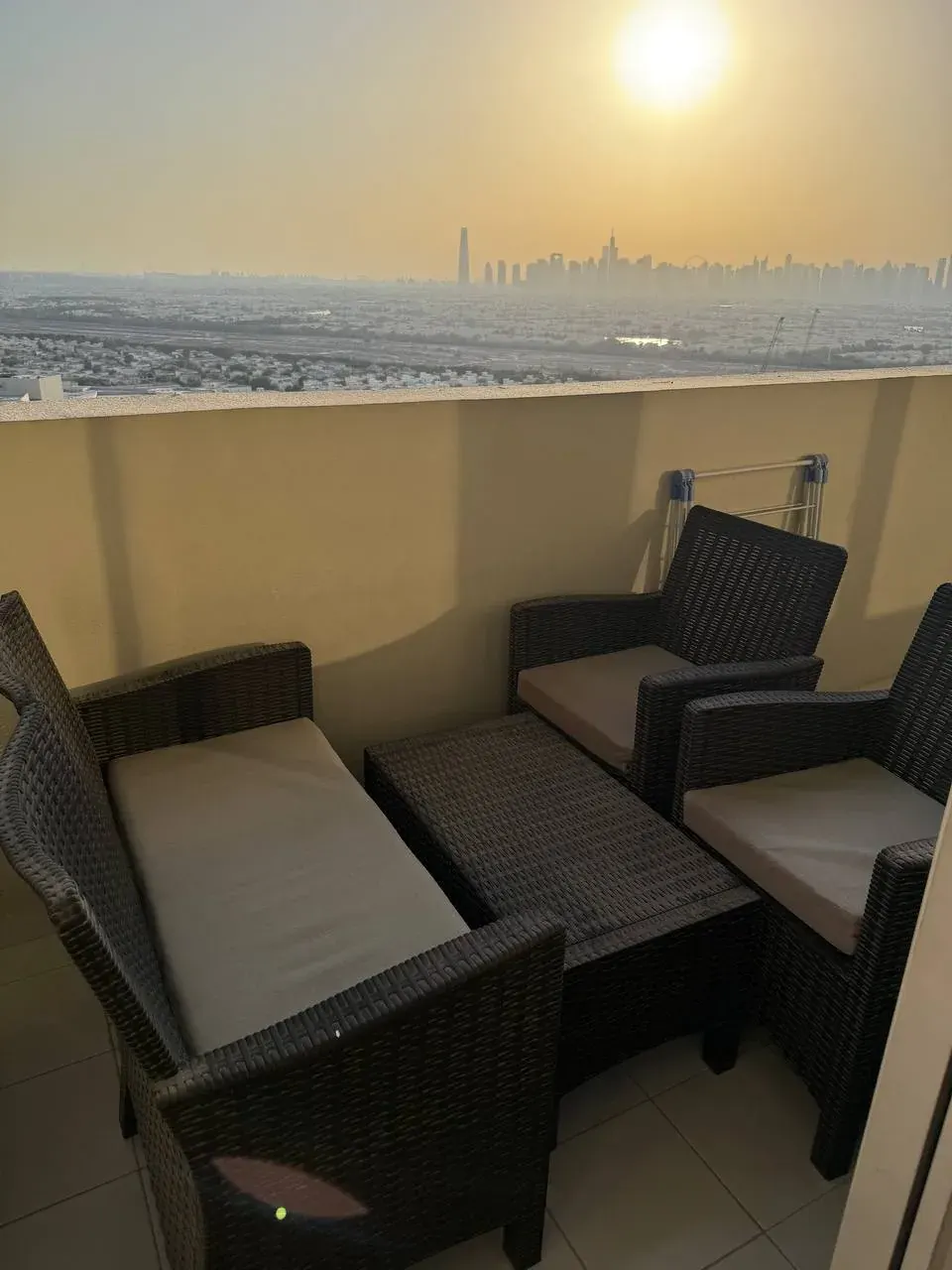 Balcony seating area with wicker patio furniture and cushions overlooking a city skyline at sunset