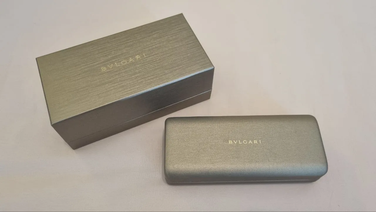 Two metallic BVLGARI-branded boxes with BVLGARI logo on a light surface Two metallic BVLGARI-branded boxes with BVLGARI logo on a light surface