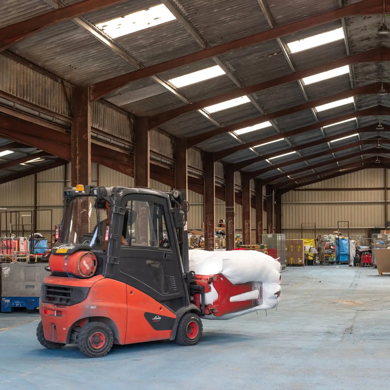 Industrial warehouse interior with a red forklift and stacked pallets of bagged goods