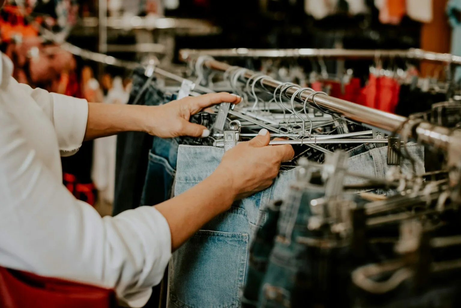 Person browsing second-hand jeans on a clothing rack in a UAE shop, representing ways to find items without paying full retail prices