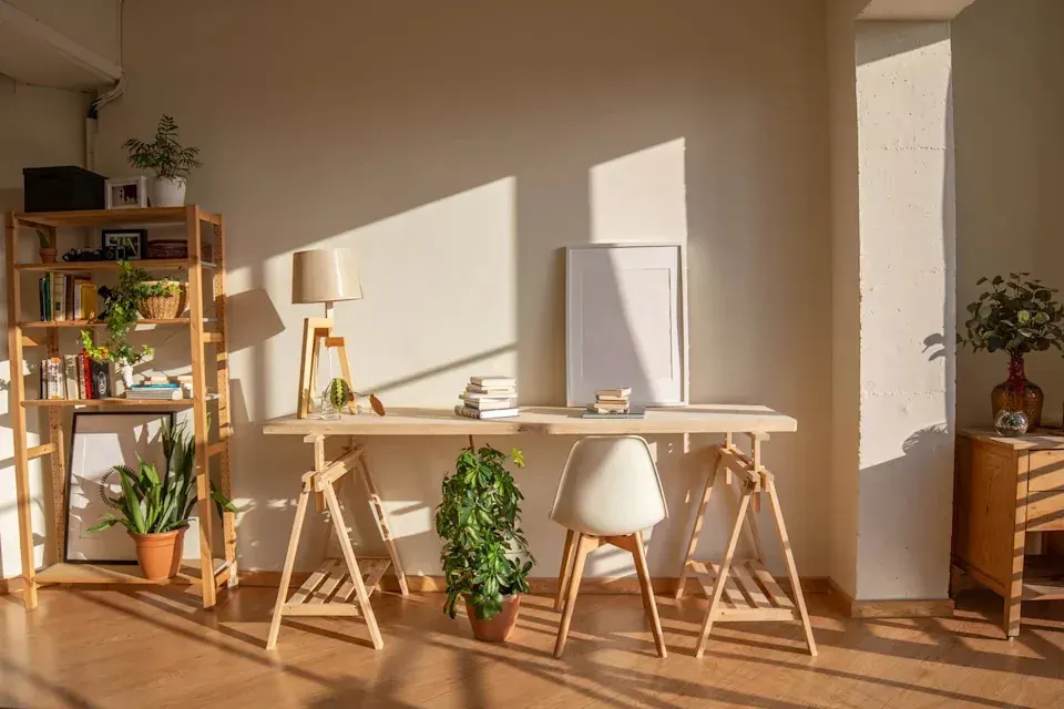 Sunlit home workspace with a wooden desk, chair, shelves, books, and plants in a UAE home study setting