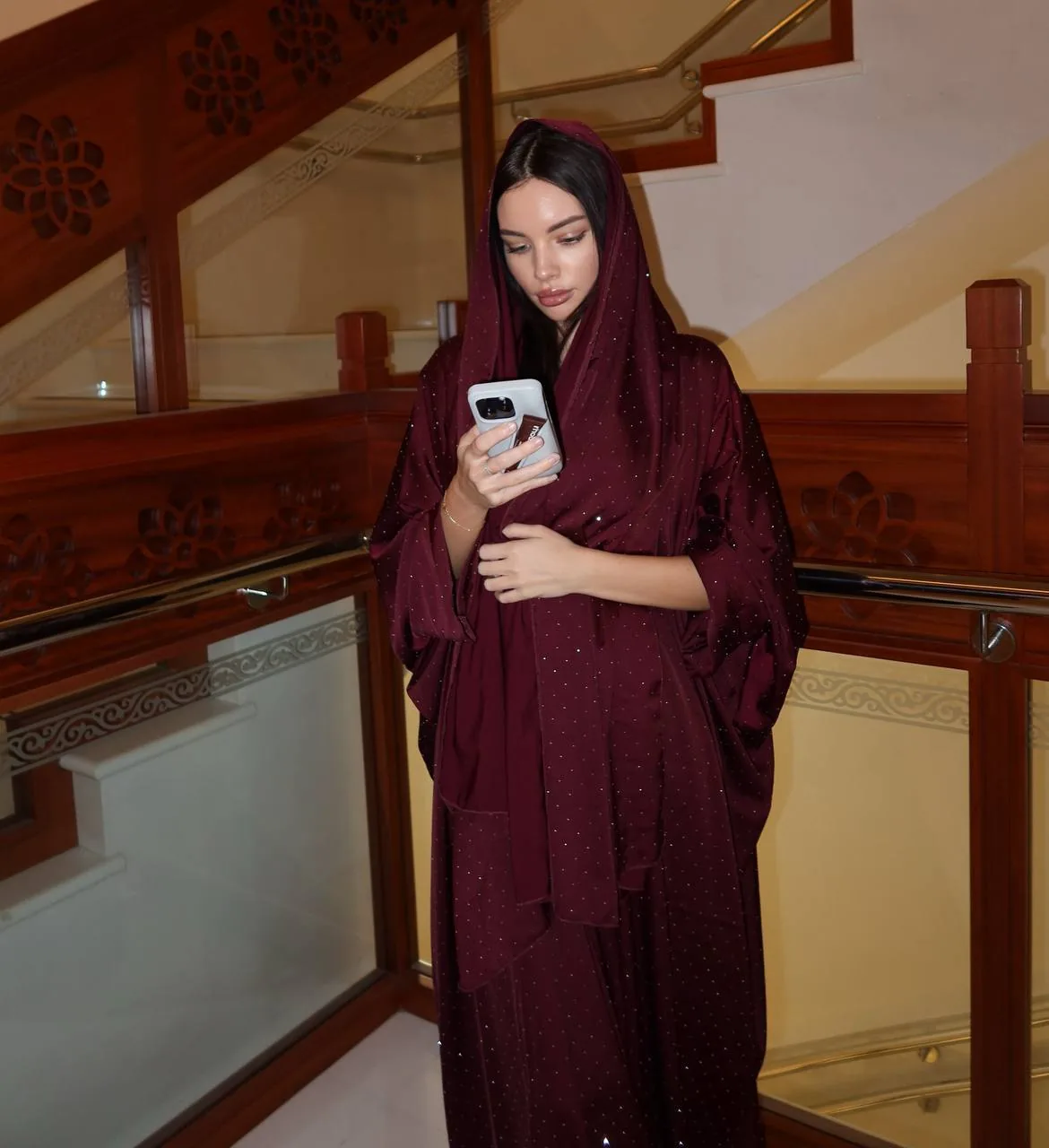 Woman in a maroon hijab using her phone indoors, representing private in-app messaging for item handovers