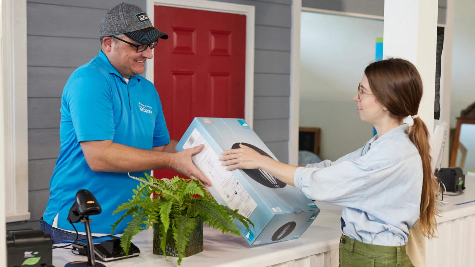 Man and woman exchanging a boxed item at a service counter, representing smooth handover of reused items in the UAE