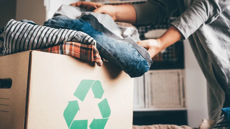 Person sorting folded clothes into a cardboard box with a recycling symbol for local reuse or disposal in Dubai