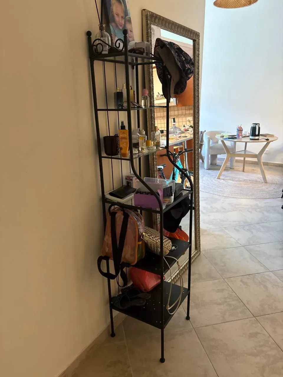 Indoor room with a metal shelf, bottles, a hanging garment, and a large framed mirror