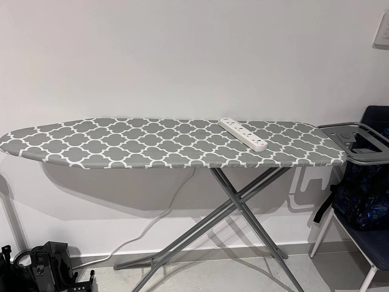 Ironing board with power strip and nearby laptop in a simple room