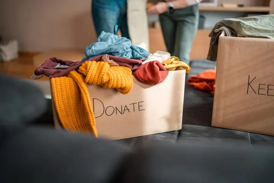Box labeled Donate with clothing and school items in a room for sorting items to keep or give away