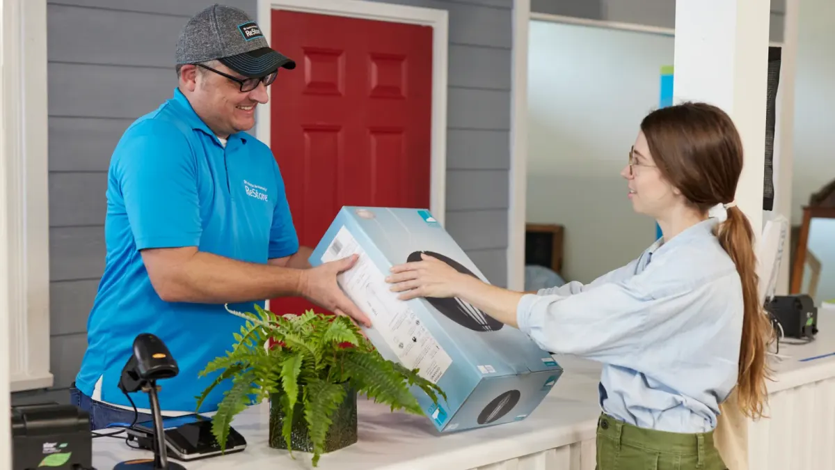 Two people exchange a boxed item at a service counter, reflecting school sports kit reuse in the UAE. Two people exchange a boxed item at a service counter, reflecting school sports kit reuse in the UAE.