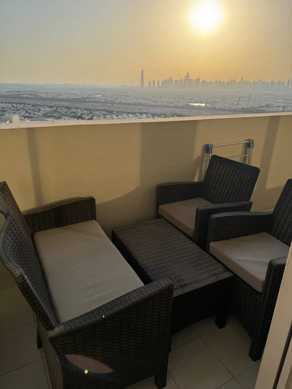 Balcony with wicker patio furniture overlooking a city skyline at sunset