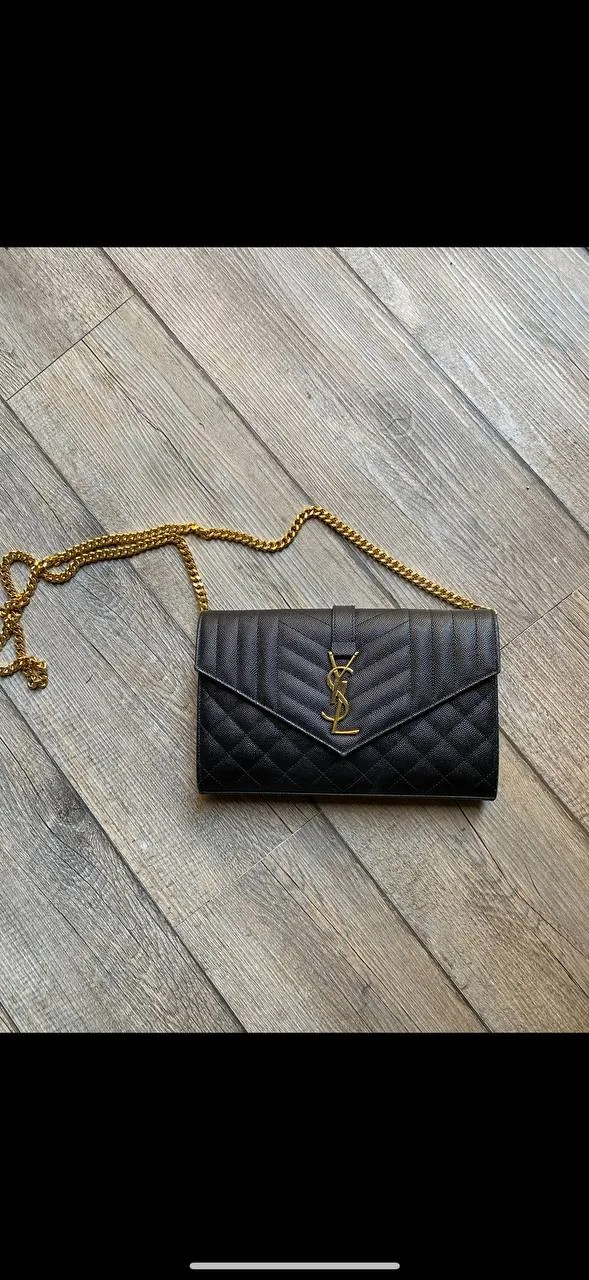 Black quilted YSL wallet-style handbag with gold chain strap on wooden floor