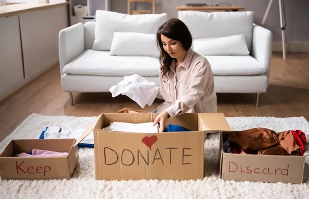Woman in a shared living room sorting boxes labeled keep, donate, and discard to declutter a co-living space