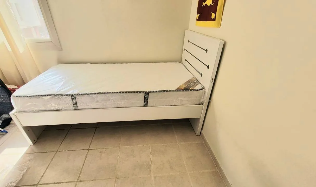 Single bed with wrapped mattress in a small, unfurnished room