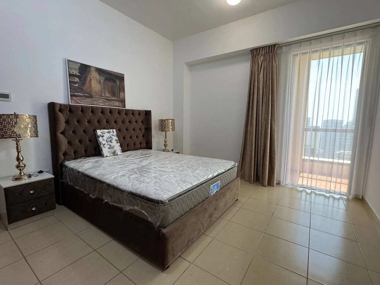 Comfortable bedroom with large upholstered bed, nightstands, and balcony door, suggesting a student dorm-style room setup